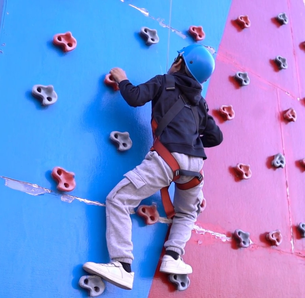 Adventurer scaling our indoor climbing wall with safety harness